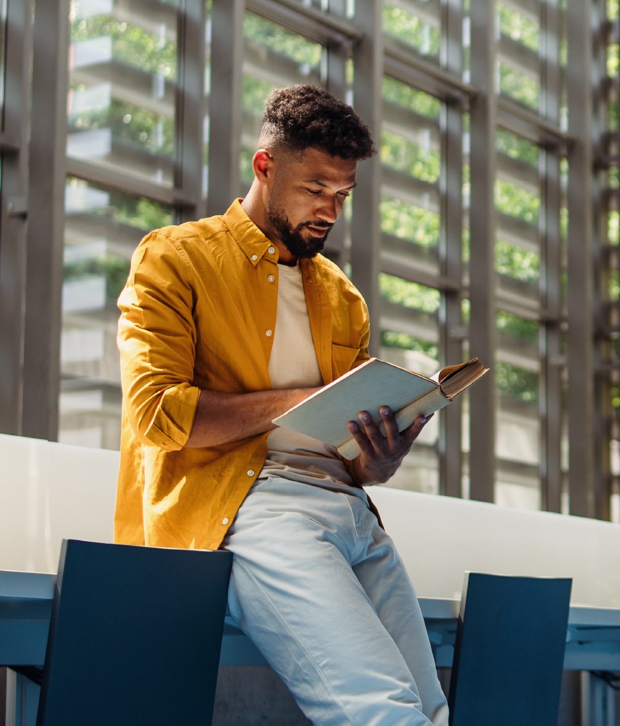 Joven trabajador que lee un libro en el vestíbulo de su oficina.