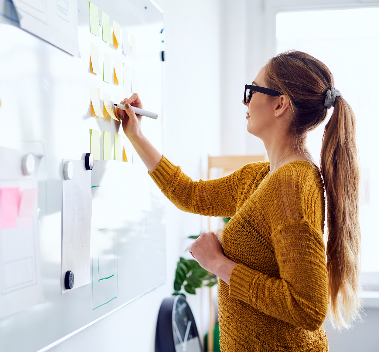 Young woman writes on a white board during a brainstorming session.